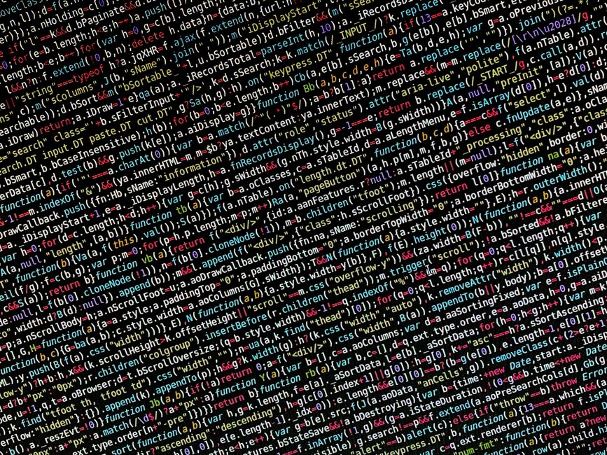A detailed close-up photograph of a computer screen displaying a dense layer of multicolored lines of programming code, primarily consisting of HTML, JavaScript, and CSS snippets. The code features va